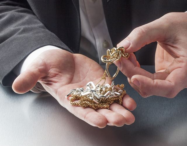 Händer som visar upp skrotguld vid trygg guldförsäljning hos Guldsmedshuset i Sävedalen