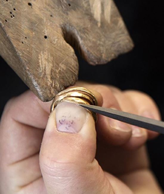 Närbild på professionell smyckesreparation hos Guldsmedshuset. Efter en storleksändring justeras och filas mönstret för hand för att återställa ringens form och finish.
